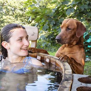 Dog with paws up on wooden hot tub looking at girl